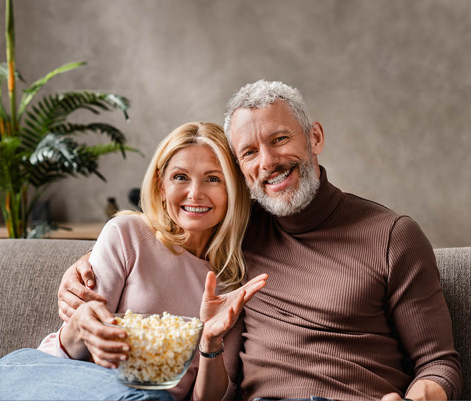 Happy middle aged couple, wife and husband watching tv and eating popcorn